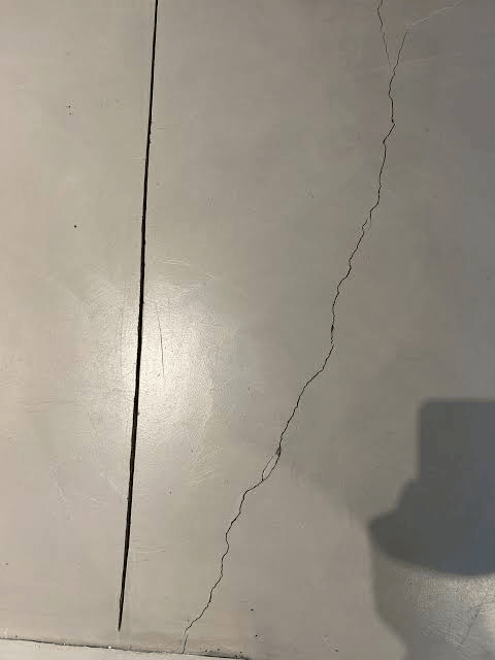 Cracked and damaged surface of a floor, showing a long straight fissure and a jagged crack.